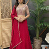 Woman in red and beige embroidered Indian lehenga with jewelry, standing indoors by plant and wooden screen