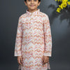 Boy wearing pink and cream Indian ethnic kurta with geometric patterns, standing against gray background with yellow flowers