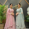 Two women wearing embroidered pink and mint green lehengas with matching jewelry, standing indoors at Anandi Fashions