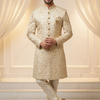 Man wearing a cream sherwani with intricate patterns against a white curtain background