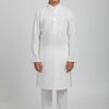 Boy wearing white embroidered Indian kurta with churidar pants, standing barefoot on plain background
