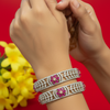 Close-up of hands wearing two ornate Indian diamond and ruby bangles against red background with yellow flowers