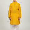 Boy wearing yellow embellished traditional Indian kurta with white churidar pants standing barefoot