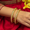 Close-up of hand wearing gold and diamond-studded bangles paired with red embroidered Indian ethnic wear and yellow flowers
