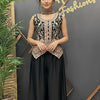 Woman in a stylish outfit standing in front of a branded wall with plants on either side.