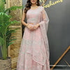 Woman in a pink traditional outfit standing in front of a decorative wall with 'Anandi Fashions' branding.