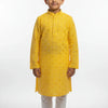 Young boy wearing yellow embroidered Indian kurta with white churidar pants standing barefoot on white background