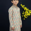 Young boy in colorful printed kurta with white pants standing against black background with yellow floral decoration