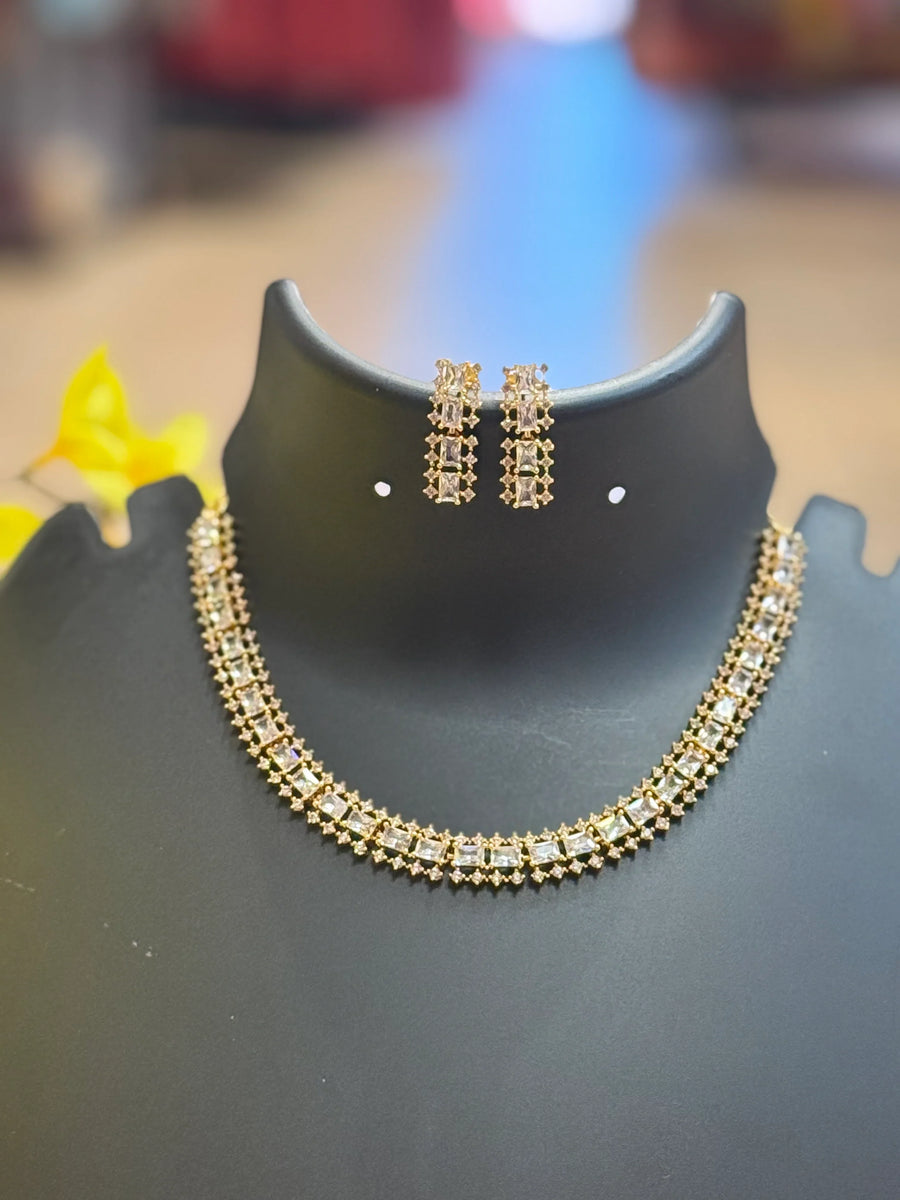 Elegant gold and white stone necklace with matching square earrings on black display