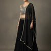 Woman wearing black Indian ethnic lehenga with silver embroidery and sheer dupatta, posing against neutral background