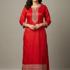 Woman wearing red Indian ethnic kurta with embroidered neckline and hem, beige shoes, standing against plain background