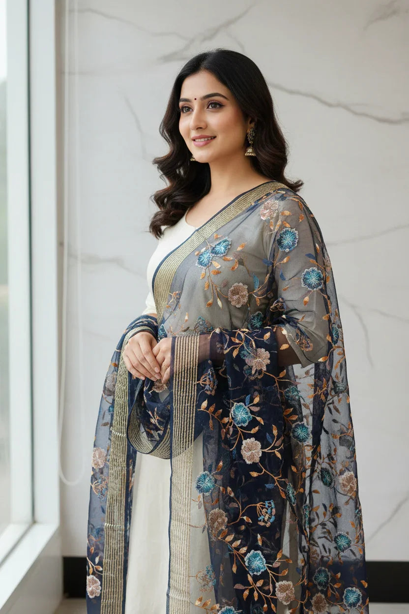 Smiling woman wearing white Indian ethnic dress with navy blue floral embroidered dupatta at window