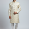 Man wearing a cream sherwani with white pants on a light gray background