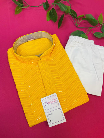 Yellow Indian ethnic men's kurta with white pants on pink background, Anandi Fashions tag, decorative green leaves