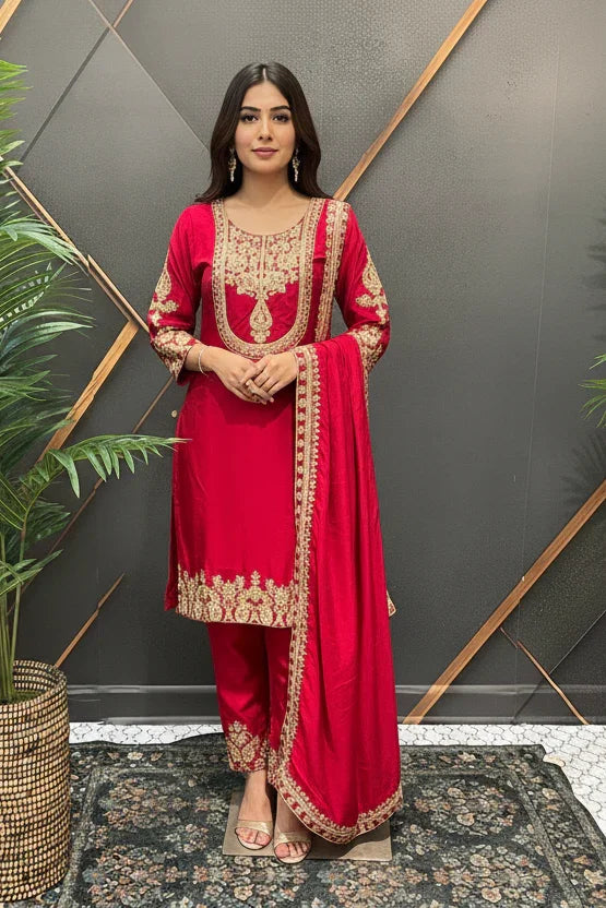 Woman wearing red Indian ethnic wear with gold embroidery, standing indoors by decorative plants