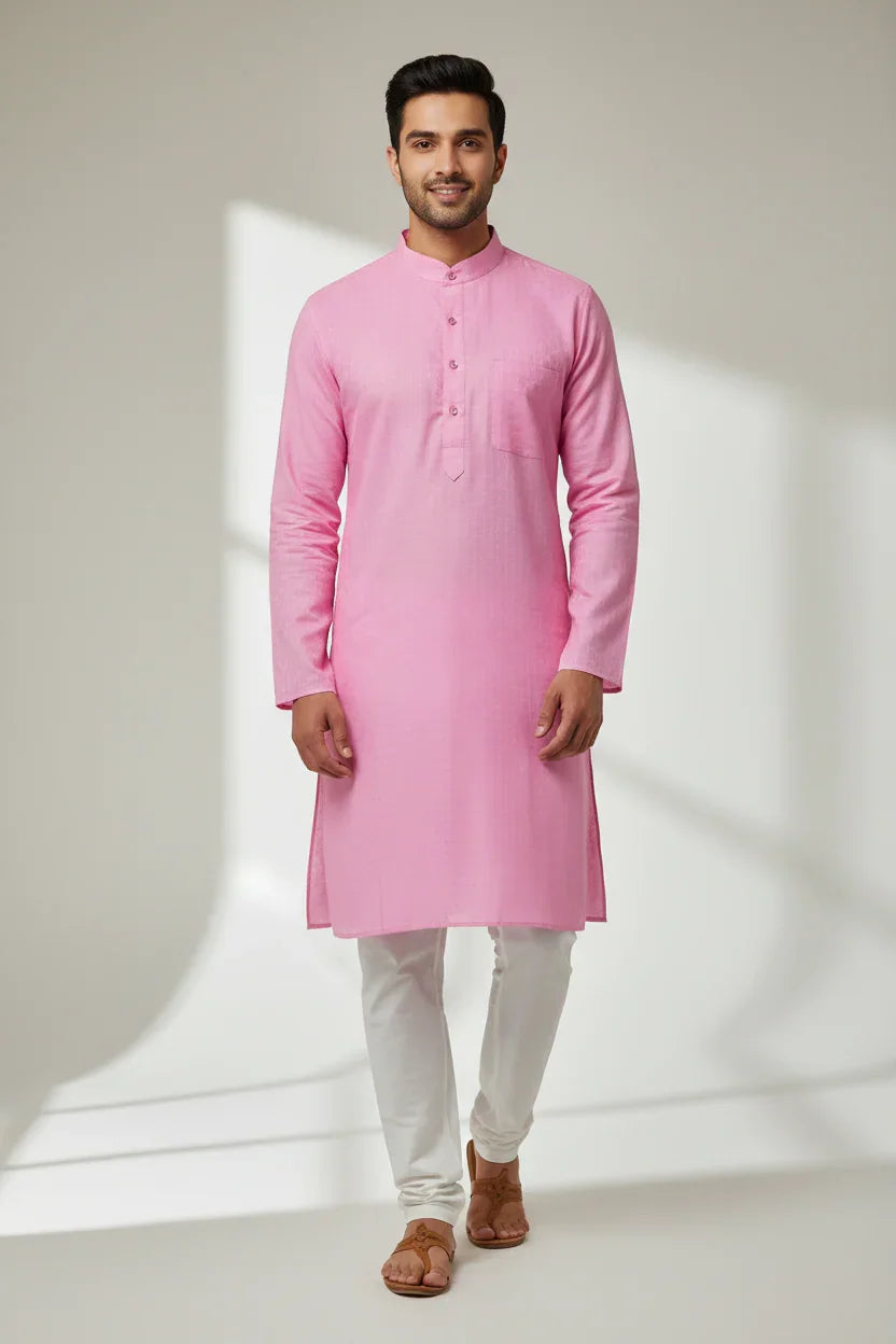 Man wearing pink cotton kurta and white churidar with brown sandals in a light studio setting