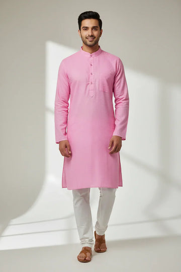 Man wearing pink cotton kurta and white churidar with brown sandals in a light studio setting