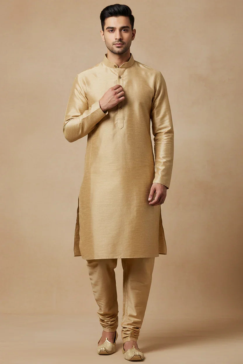 Man wearing golden silk Indian ethnic kurta pajama with jutti shoes on beige background