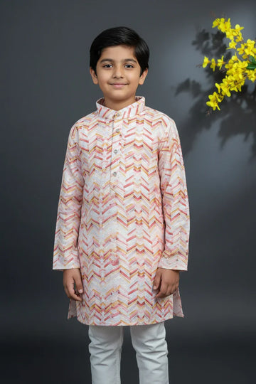 Boy wearing pink and cream Indian ethnic kurta with geometric patterns, standing against gray background with yellow flowers