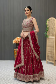 Woman in a maroon Indian ethnic lehenga with intricate gold embroidery, matching dupatta and traditional jewelry, indoors
