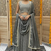 Woman in gray embellished lehenga with matching dupatta and earrings, standing in front of wooden decorative screen with marigold garlands