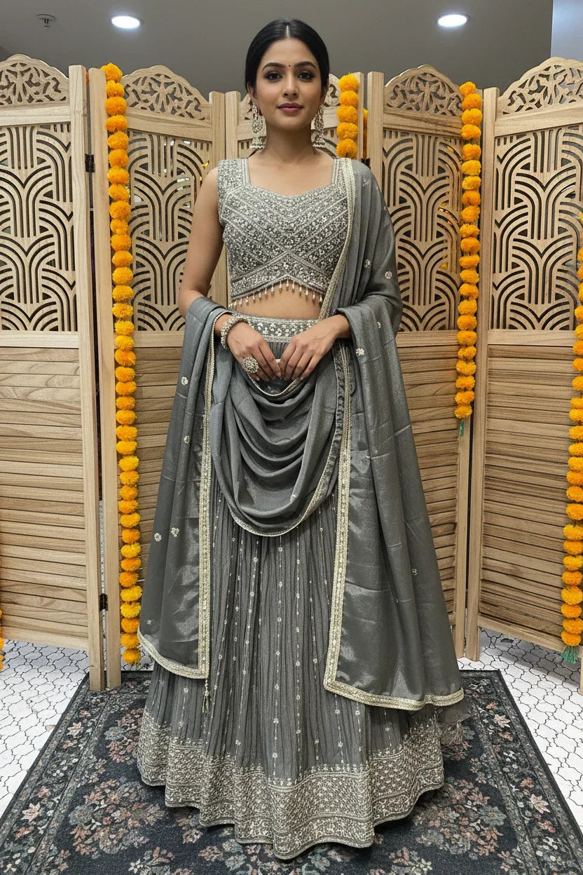 Woman in gray embellished lehenga with matching dupatta and earrings, standing in front of wooden decorative screen with marigold garlands