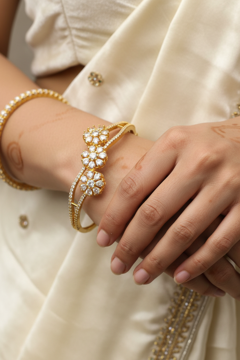 Close-up of a woman's hands wearing a gold and diamond floral bracelet and bangles, dressed in an elegant ivory saree with embellishments
