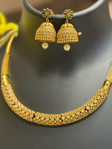 Gold Indian ethnic necklace and matching jhumka earrings with green floral accents and pearl drops on black display