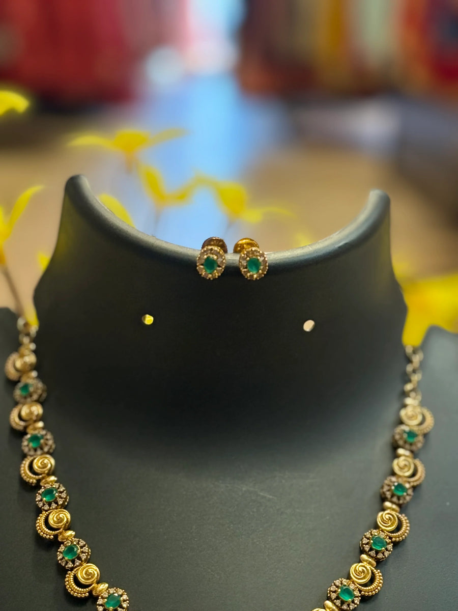 Gold and green gemstone necklace with matching stud earrings displayed on a black stand, elegant ethnic jewelry