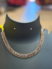 Elegant gold necklace with rectangular purple gemstones displayed on black jewelry stand at Anandi Fashions