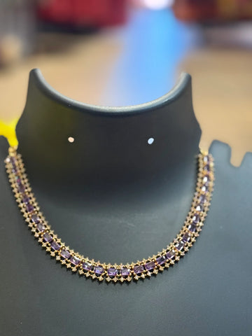 Elegant gold necklace with rectangular purple gemstones displayed on black jewelry stand at Anandi Fashions
