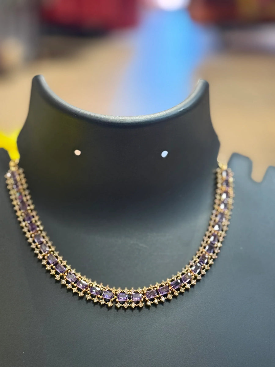 Elegant gold necklace with rectangular purple gemstones displayed on black jewelry stand at Anandi Fashions