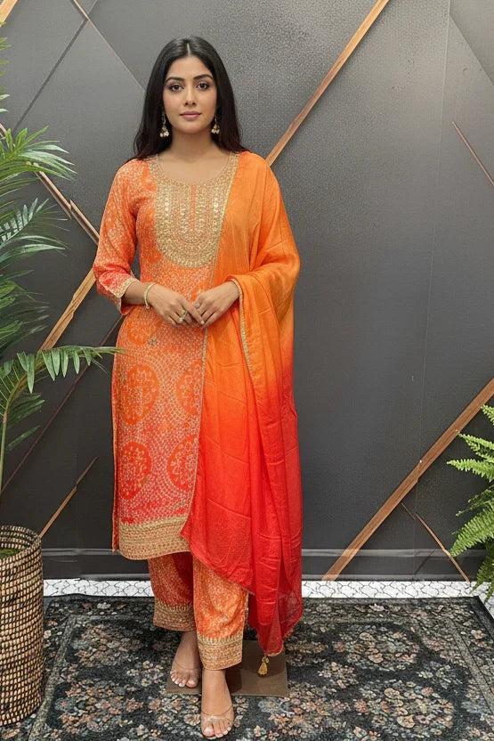 Woman in vibrant orange Indian ethnic wear with gold embroidery, including kurta, pants, and matching dupatta