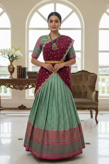 Model wearing elegant green and maroon Indian ethnic lehenga with intricate embroidery, gold jewelry in bright indoor setting
