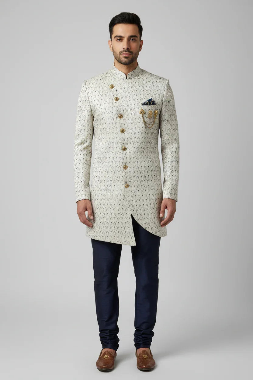 Man wearing cream embroidered Indian sherwani with navy churidar pants and brown traditional shoes