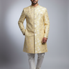 Man wearing a traditional beige sherwani with white pants on a gray background