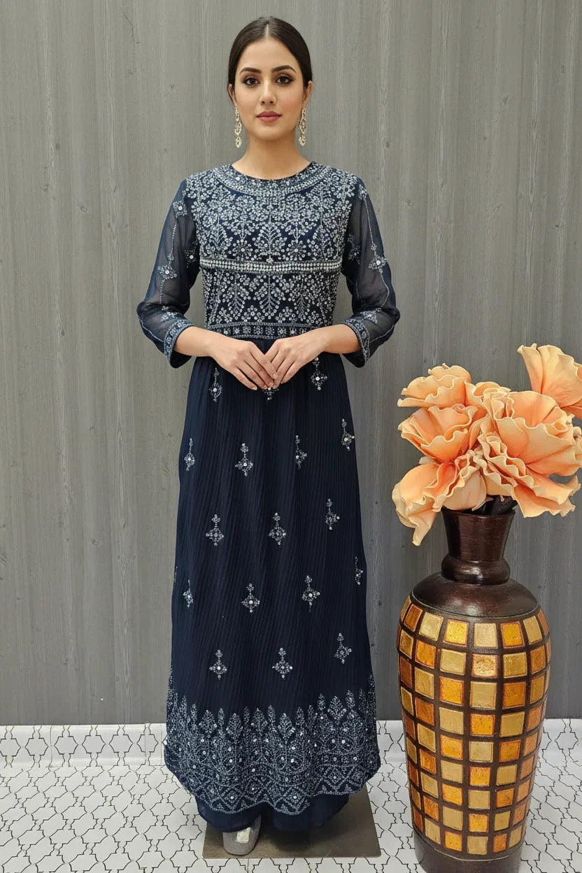 Woman wearing navy blue Indian ethnic dress with intricate white embroidery standing by decorative vase with orange flowers