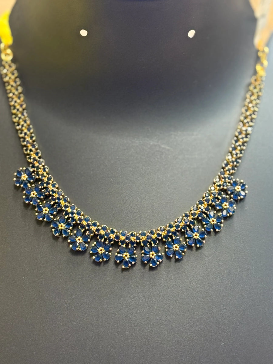 Elegant Indian gold necklace with blue flower-shaped stones displayed on black stand