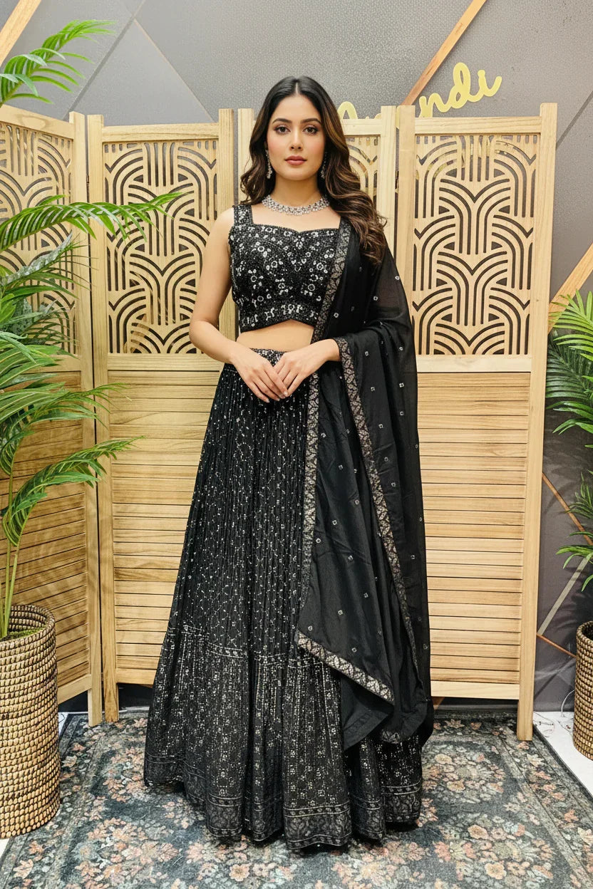 Woman in black sequin lehenga, choli, and dupatta posing indoors with decorative wooden screen and plants