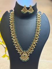 Gold-toned Indian ethnic jewelry set with green bead and stone accents displayed on black stand