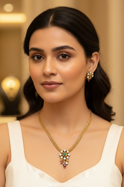 Close-up of a woman wearing a gold necklace and matching earrings with green, white, and red gemstones at Anandi Fashions