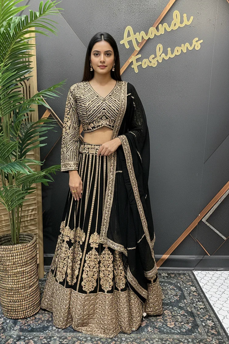 Woman in black and gold embroidered lehenga posing in front of Anandi Fashions boutique wall