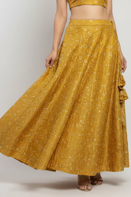 Woman wearing mustard yellow Indian ethnic skirt with floral embroidery and matching blouse, styled with sandals