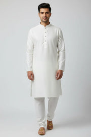 Man wearing elegant white Indian kurta with churidar and tan traditional sandals, studio background