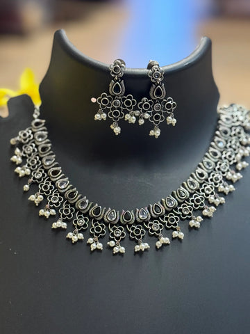 Oxidized silver ethnic necklace and matching floral earrings with pearl details displayed on black stand
