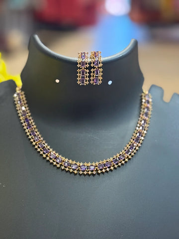 Elegant gold necklace and matching earrings set adorned with purple gemstones on black display stand