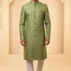 Man wearing a green patterned kurta with white pants against a beige wall.
