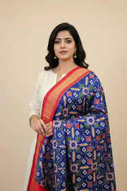 Indian woman wearing white kurta and vibrant blue saree with colorful floral patterns and red-gold border