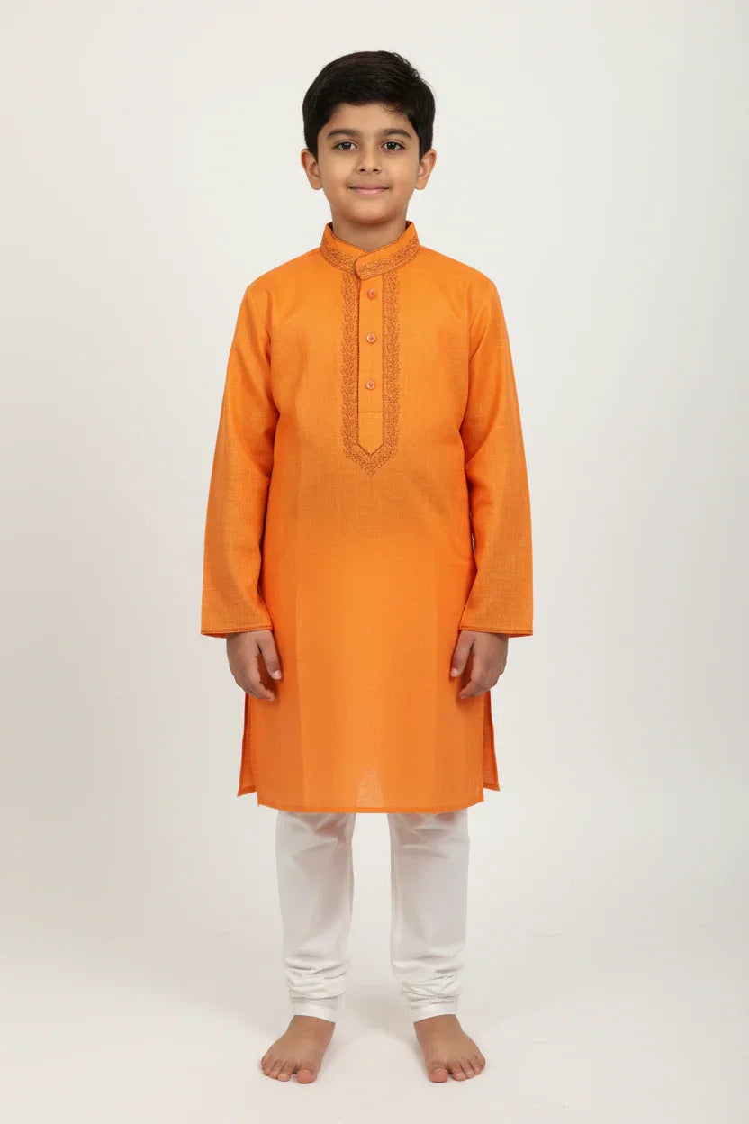 Boy wearing vibrant orange embroidered kurta with white churidar pants in studio
