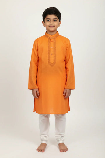Boy wearing vibrant orange embroidered kurta with white churidar pants in studio